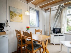 Ein gemütliches Zimmer mit einem Holztisch, Stühlen, einem Gemälde, einer Kaffeemaschine, einem Fernseher und einer Leiter.