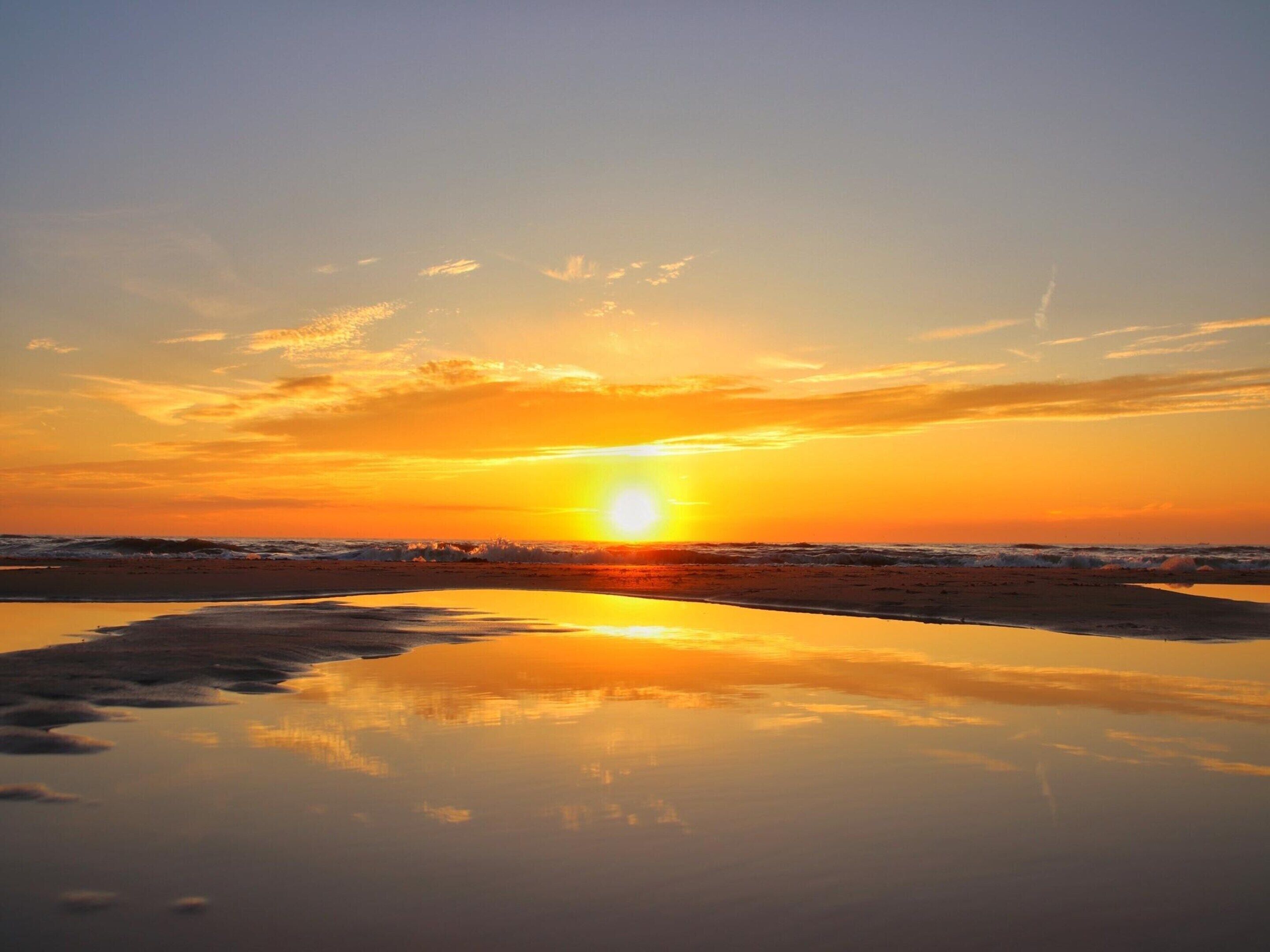 A sunset over a beach with calm water reflecting the sky.