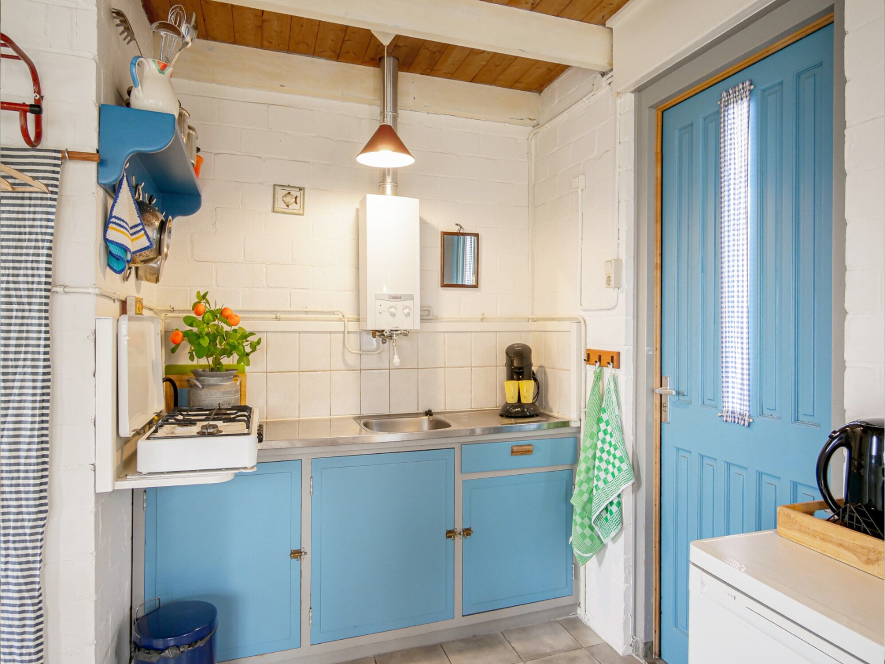 Une cuisine de taille réduite avec une porte bleue, des murs blancs, un luminaire suspendu et une cuisinière.