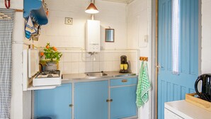 A compact kitchen with a blue door, white walls, a hanging light fixture, and a stove. - Pet-friendly Home in Callanstoog Near Beach (Callantsoog)