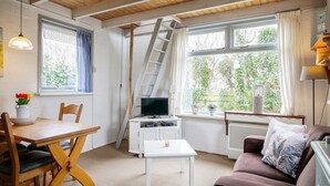 A cozy room with a wooden ceiling, a TV on a white cabinet, a dining table with chairs, a sofa, and a window with curtains. - Pet-friendly Home in Callanstoog Near Beach (Callantsoog)