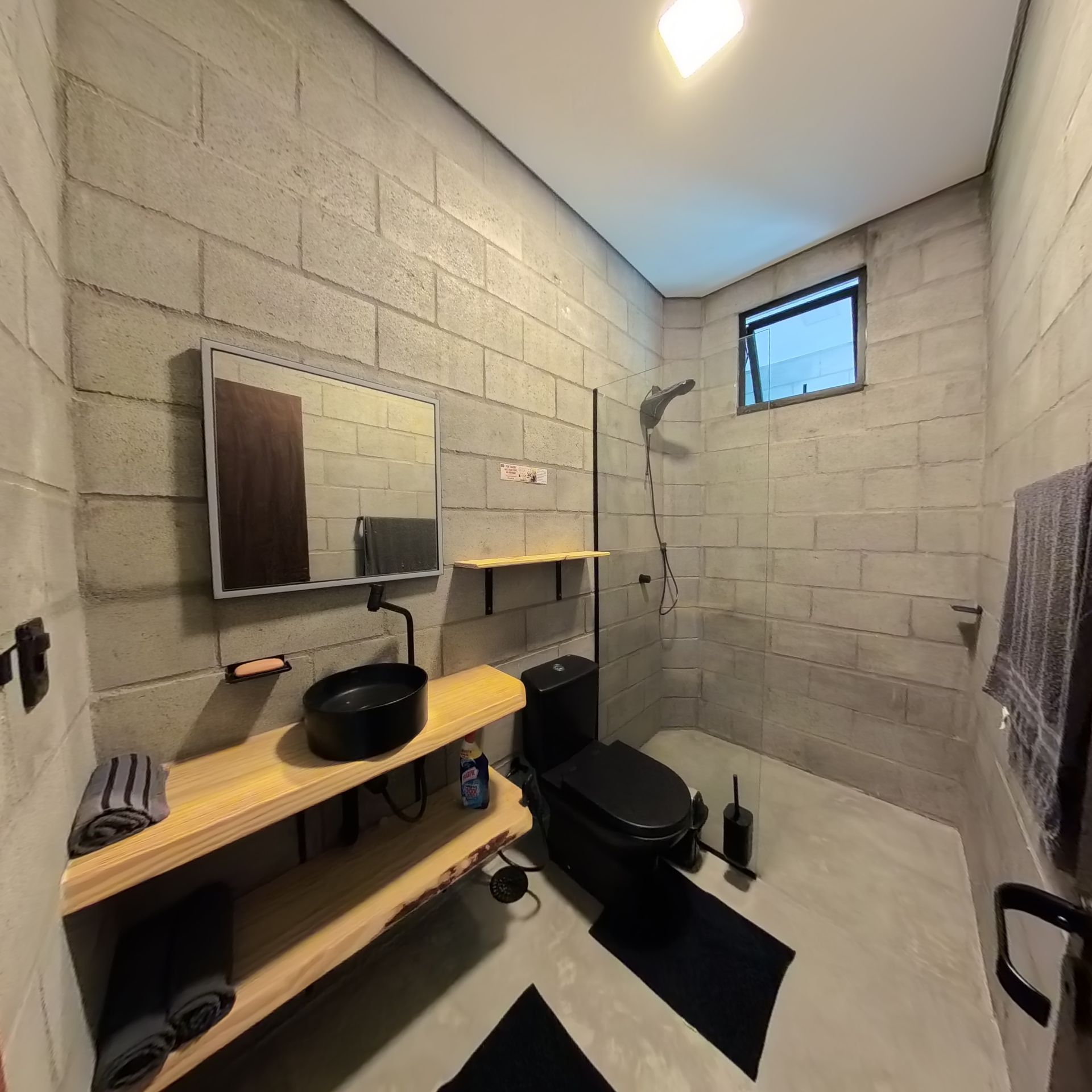 Ein kleines Badezimmer mit Dusche, Spiegel, Waschbecken mit schwarzer Schüssel und Toilette.