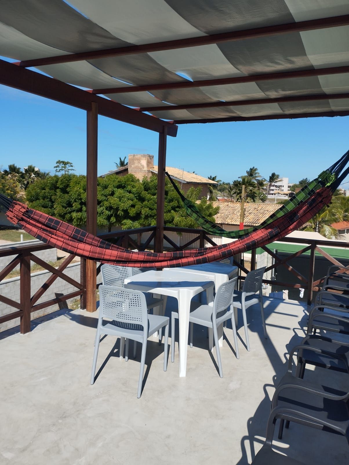 A covered outdoor seating area with tables and chairs, a hammock, and a view of buildings and trees.
