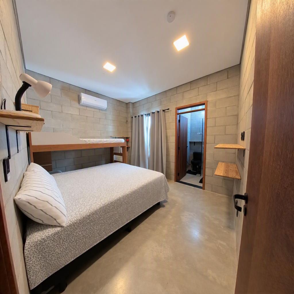 Une chambre avec un lit superposé, une table de chevet, une lampe et une porte donnant sur une salle de bain.
