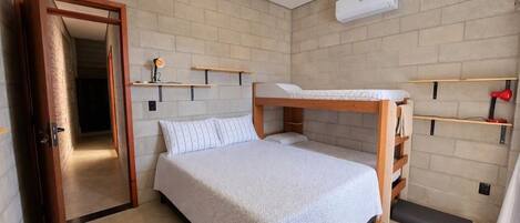 Un dormitorio con una cama litera, una mesita de noche, una lámpara y un aire acondicionado instalado en la pared.