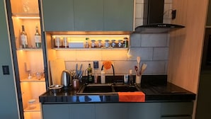 A compact kitchen with a built-in oven, a sink, and a range hood. There are shelves above the sink with jars and bottles. - A Green House in Aguas Belas (Caponga)