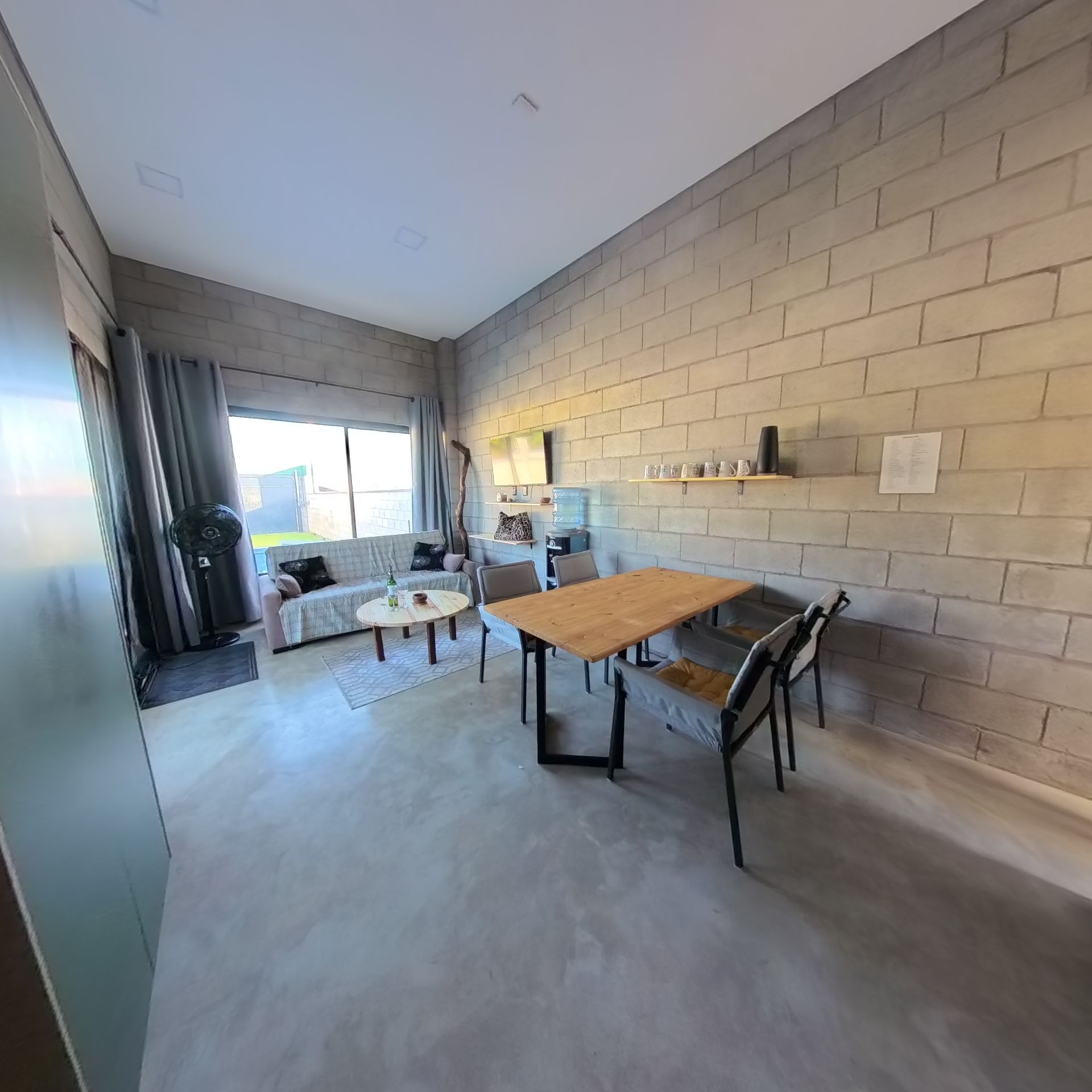A modern living room with a dining area, featuring a brick wall, a sofa, a coffee table, and a wooden dining table.