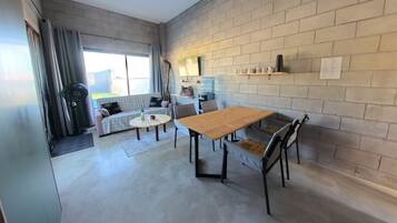 A modern living room with a dining area, featuring a brick wall, a sofa, a coffee table, and a wooden dining table.