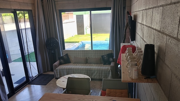 A room with a wooden table, a sofa, a fan, and a view of a swimming pool. - A Green House in Aguas Belas (Caponga)