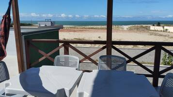 Une terrasse avec des chaises et des tables en plastique blanc, donnant sur une plage et l’océan.