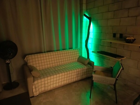 A room with a sofa, a chair, a fan, and a wall-mounted shelf.