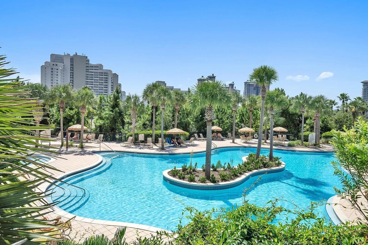Una piscina de resort con palmeras y sillas de descanso, rodeada de edificios altos.