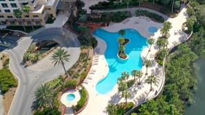 An aerial view of a resort with a large swimming pool, palm trees, and a curved road. - New Listing: Awesome Views Luau SanDestin Resort (Destin)