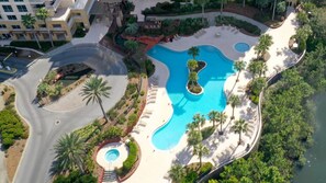 Eine Vogelperspektive eines Resorts mit einem großen Schwimmbad, Palmen und einer gewundenen Zufahrtsstraße.