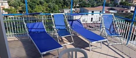 A balcony with blue lounge chairs and a white chair, overlooking a residential area.