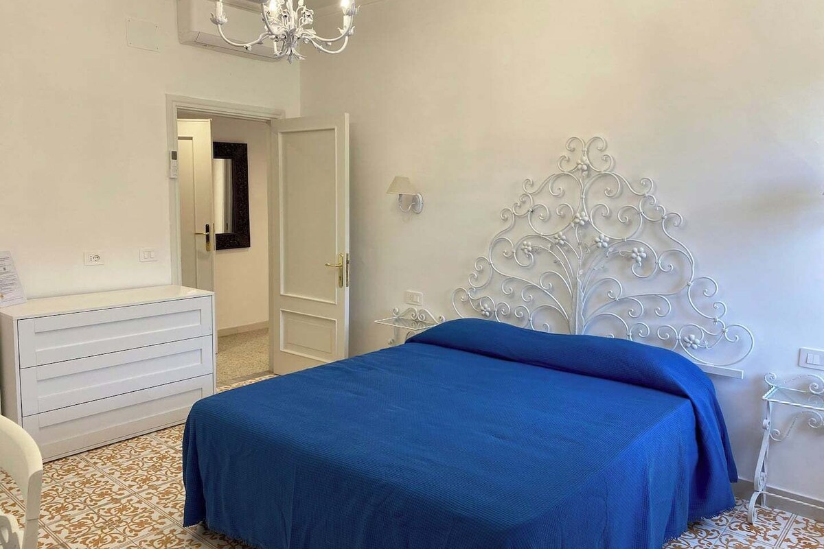 Un dormitorio con cama, cómoda, candelabro y puerta que da a otra habitación.