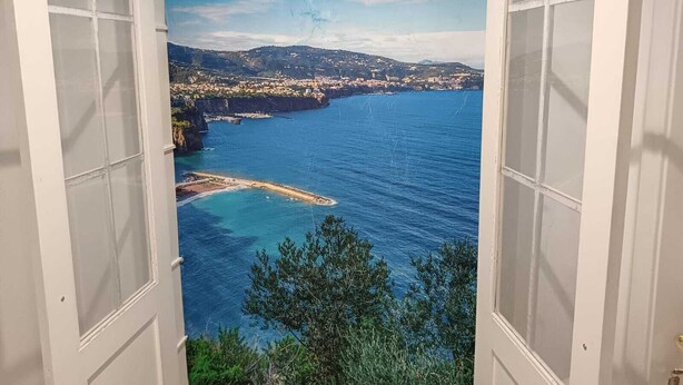 Une vue sur la côte, aperçue à travers une fenêtre, avec un ciel dégagé, une plage et une ville au loin.