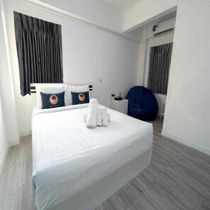 Ein Hotelzimmer mit einem großen Bett, einem Sessel, einem Schreibtisch und einem Fenster mit Vorhängen.