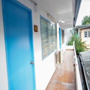 Ein Korridor mit einer blauen Tür, einem Fenster mit Rollläden und einem gefliesten Boden.