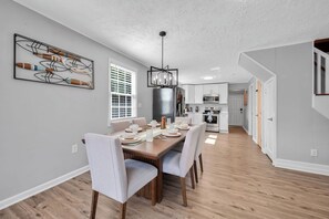 Une cuisine moderne avec des meubles blancs, un réfrigérateur noir et un coin repas comprenant une table et des chaises en bois.