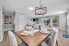 A dining area with a wooden table set for four, a modern chandelier, and a view of a body of water through large windows. - Luxury Lakefront Retreat with Private Dock ,Sleeps 16 (Lake Harmony)