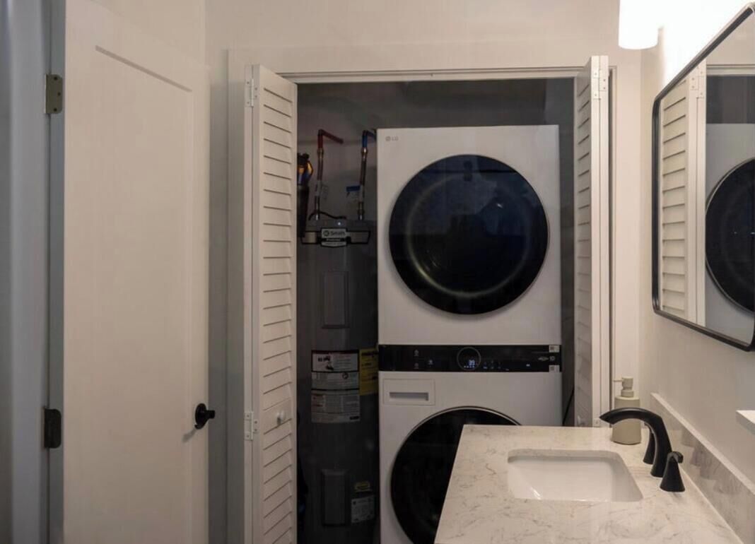 A compact laundry room with two stacked washing machines, a sink, and a mirror.