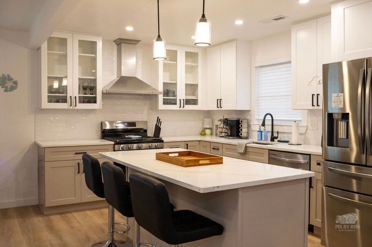 A modern kitchen with white cabinetry, a central island with bar stools, stainless steel appliances, and pendant lighting.
