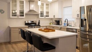 A modern kitchen with white cabinetry, a central island with bar stools, stainless steel appliances, and pendant lighting. - Villas House - 10 mins to Cape May, 15 to Wildwood (Lower Township)