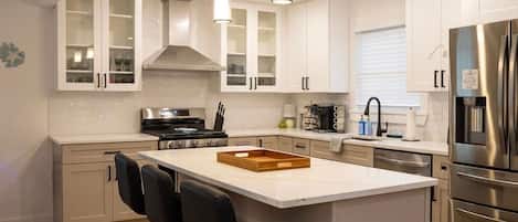 A modern kitchen with white cabinetry, a central island with bar stools, stainless steel appliances, and pendant lighting.