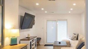 A modern living room with a sofa, a coffee table, a TV mounted on the wall, and a sliding glass door leading to an outdoor area. - Villas House - 10 mins to Cape May, 15 to Wildwood (Lower Township)