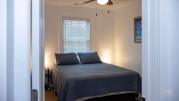 A bedroom with a bed, a ceiling fan, a window with blinds, and a nightstand. - Villas House - 10 mins to Cape May, 15 to Wildwood (Lower Township)