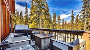 Eine Terrasse mit Sitzgelegenheiten im Freien, einer Feuerstelle und Blick auf einen bewaldeten Gebirgszug.