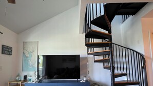 Een woonkamer met een blauwe entertainmentkast, een flatscreen televisie, een kaart aan de muur, een trap en een kleine tafel met een vaas.
