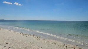 Een strand met helder water, een zandstrand en een verre kustlijn.