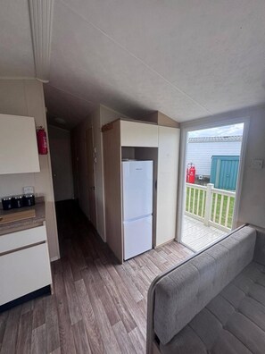 A compact kitchen with a refrigerator, cabinets, and a countertop with tea and coffee containers. - Seaside Retreat Ingoldmells (Skegness)