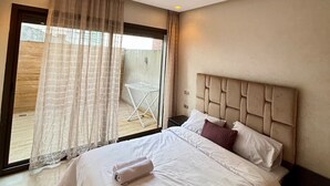 Ett hotellrum med en stor säng, en sänggavel, ett fönster med gardiner och utsikt över omgivningen.