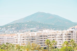 A multi-story building with balconies, a mountain in the background, and palm trees in the foreground. - Ac152 - Top Renovated Modern 1 Bed With Pool (Marbella)
