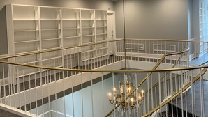 Tilava sisustus, jossa on keskeisellä paikalla sijaitseva portaikko, koristeellinen kattokruunu ja valkoinen hyllykkö.