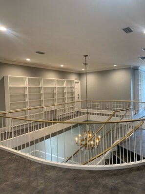 Ein geräumiger Innenraum mit einer zentralen Treppe, einem Chandelier und einem weißen Bücherregal.