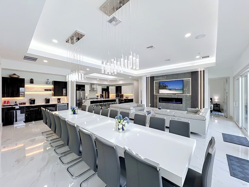 A modern kitchen with a central island, a dining area with a long table, and a TV mounted on the wall.