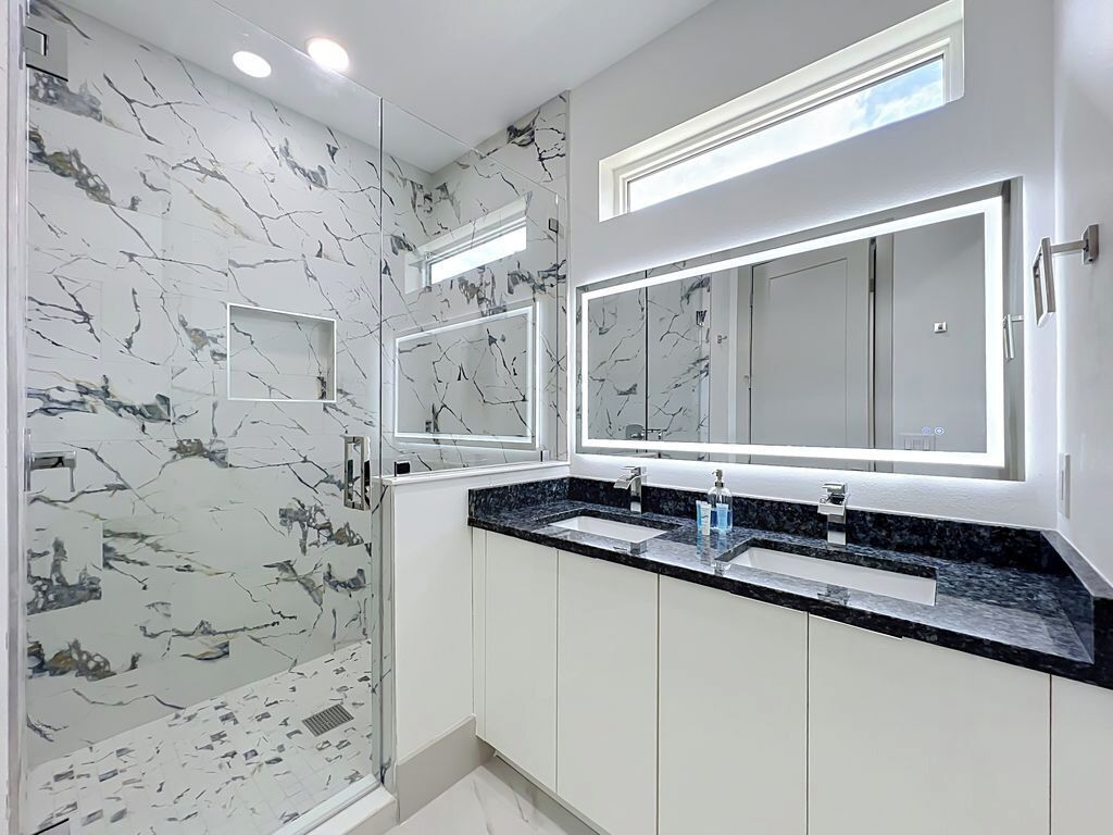 A bathroom with a marble backsplash, dual sinks, and a large mirror.