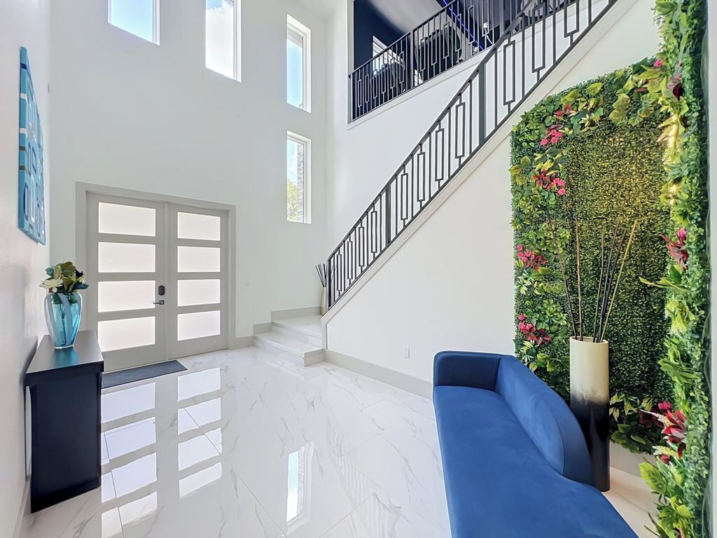 Un intérieur spacieux avec un escalier, un canapé bleu et un mur décoratif agrémenté de plantes.