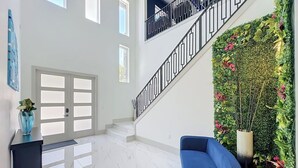 Un interior espacioso con una escalera, un sofá azul y una pared decorativa con plantas.