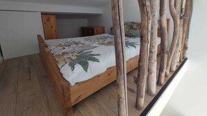 Ein Schlafzimmer mit einem hölzernen Bett, einer weißen Decke und einer schrägen Deckenkonstruktion.