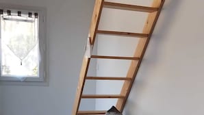 Ein Zimmer mit einer Holzleiter an der Wand, einer Couch mit Tarnabdeckung und einem Fenster mit Vorhängen.