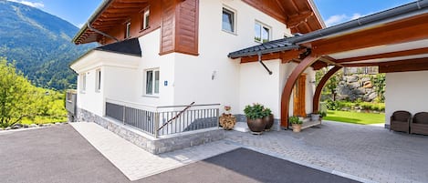 A two-story house with a wooden roof, a covered porch, and a stone wall.