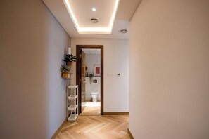 Ein Flur mit Holzboden, einer weißen Tür zu einem Badezimmer und einem Regal mit Pflanzen.