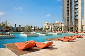 Ein Schwimmbecken mit Liegestühlen, ein großes Gebäude mit einer Kuppel und ein hohes Hotelgebäude.