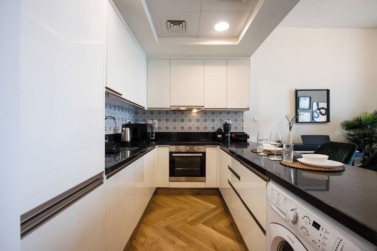 A modern kitchen with white cabinets, a built-in oven, and a washing machine.