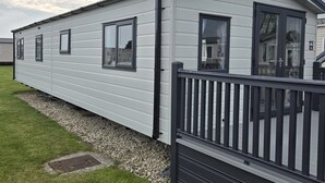 A mobile home with a black railing, large windows, and a gravel driveway.